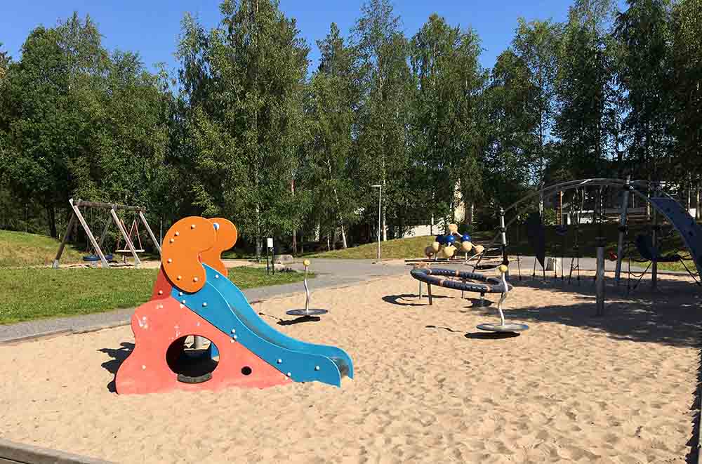 Färgglad liten rutschkana med klätterredsakp i bakgrunden. Underlaget är sand