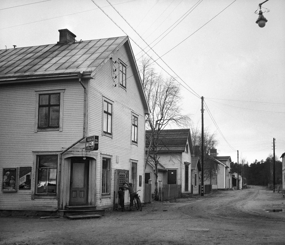 Oasfalterad gata med trähus. I närmaste hörnhuset ingången till en butik.