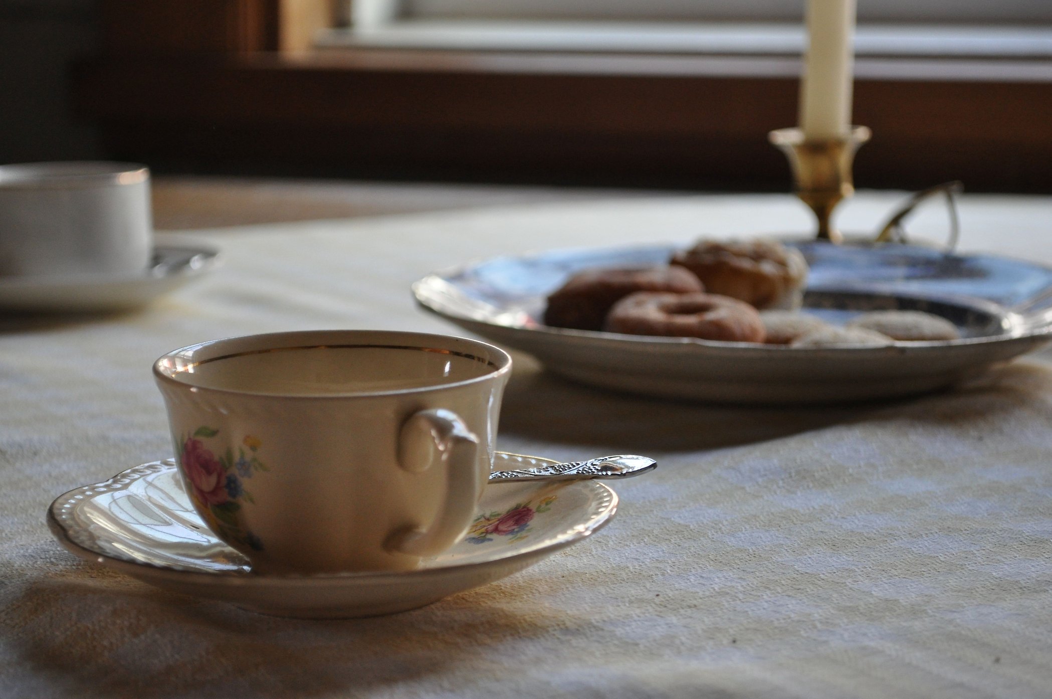 Gammal kaffekopp, kakfat och ljusstake på rutig duk.